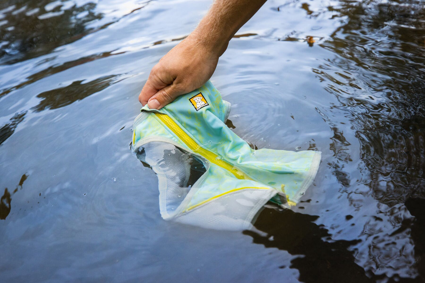 a person dunking a ruffwear cooling vest in cold water