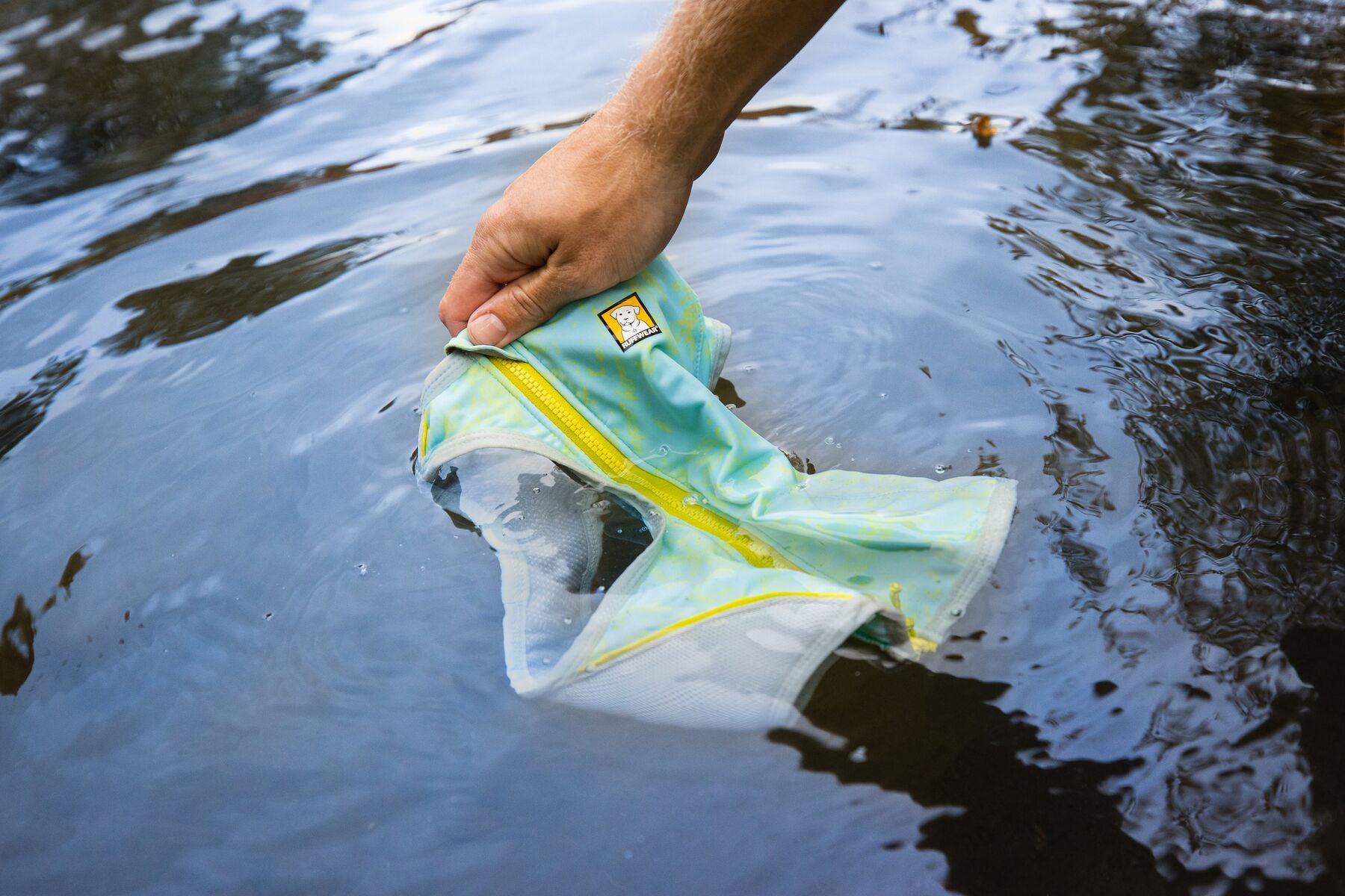 a person dunking a ruffwear cooling vest in cold water